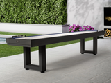 American Heritage Lanai 12' Shuffleboard Table in Obsidian Black on patio with lush greenery.