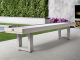 American Heritage Lanai 9' Outdoor Shuffleboard Table in Pearl White on patio with flowers and hedge.