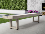 American Heritage Lanai 9' Outdoor Shuffleboard Table in Oyster Grey on a patio with greenery.
