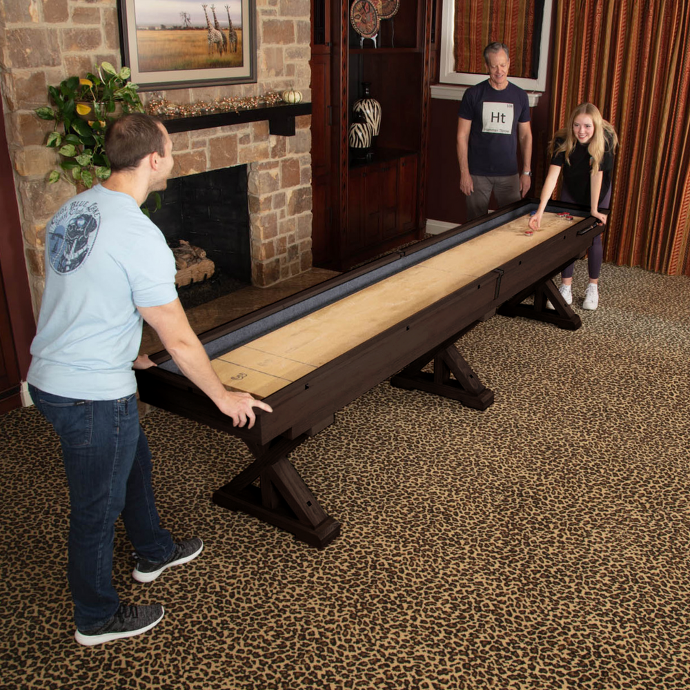 Two people playing shuffleboard in a living room with a fireplace and wooden walls.